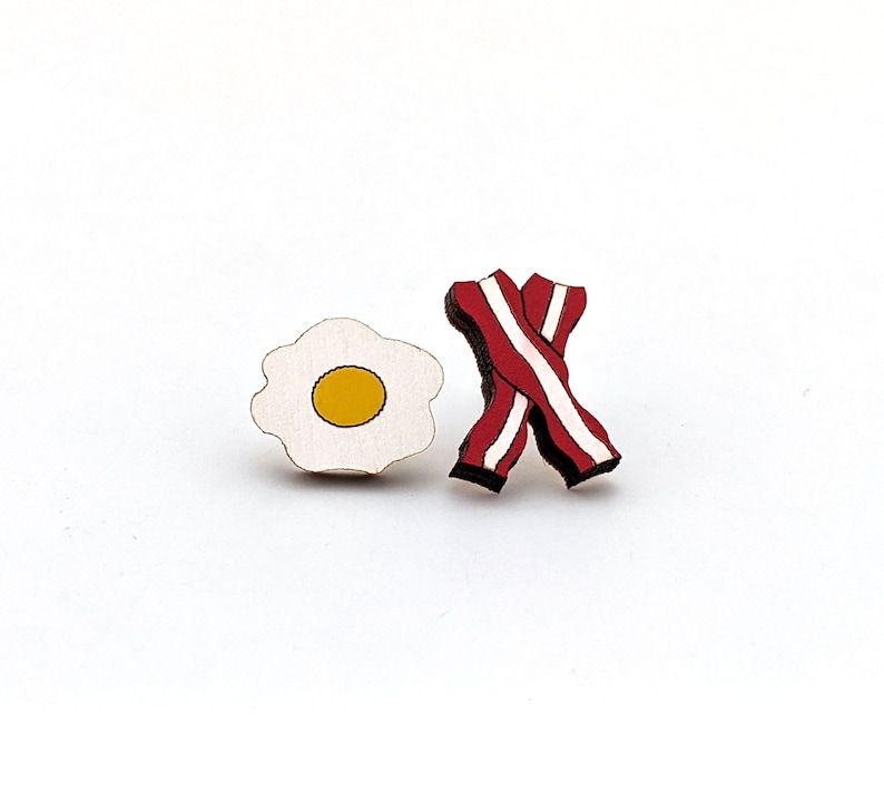 May include: Wooden cutout of a fried egg and bacon, both in red, white, and yellow colors.