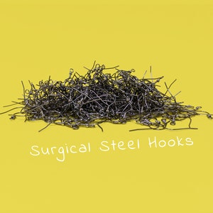 May include: A pile of surgical steel earring hooks against a bright yellow background. The hooks are silver-colored and have a curved design with a small ball at the end. The text "Surgical Steel Hooks" is written in white.