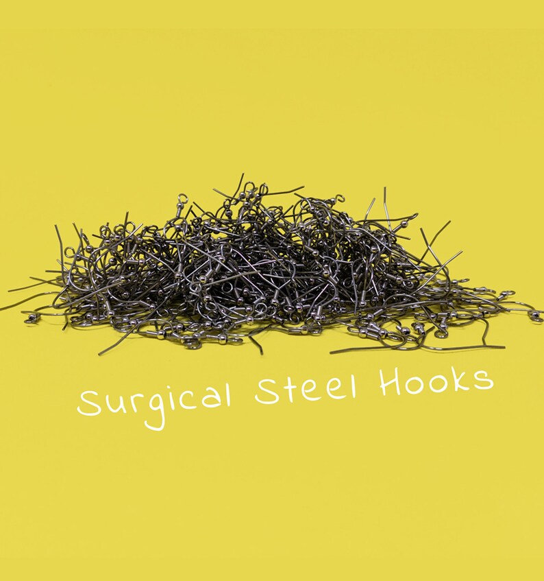 May include: A pile of surgical steel earring hooks against a bright yellow background. The hooks are silver-colored and have a curved design with a small ball at the end. The text "Surgical Steel Hooks" is written in white.
