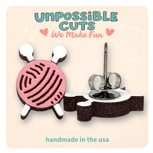 May include: A pair of stud earrings shaped like a pink yarn ball with white knitting needles. The display card features the text UNPOSSIBLE CUTS We Make Fun and handmade in the usa. The earrings have a dark brown side profile and metal posts.