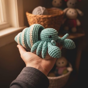 Op de afbeelding: Een handgemaakt gehaakt speelgoed, een heremietkreeft in turquoise en crème. De krab komt uit een gestreepte schelp. Het speelgoed is zacht en knuffelig, geschikt voor kinderen of als decoratie.
