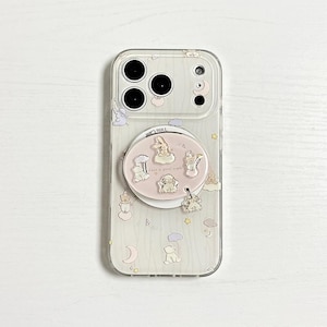 Può includere: Custodia trasparente per telefono con un design stravagante con conigli dei cartoni animati, nuvole e stelle. Un supporto a forma di cerchio rosa con illustrazioni di conigli e la scritta "have a good night" è attaccato. La custodia ha un ritaglio per la fotocamera.