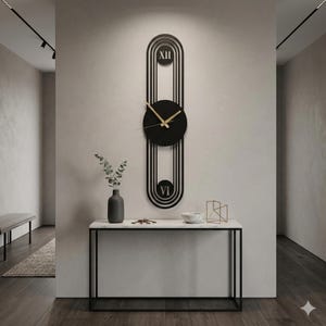 May include: A modern black wall clock with gold hands, featuring a unique elongated design with Roman numerals. The clock is mounted on a light-colored wall above a marble-topped console table. The clock's dimensions are approximately 36 inches in height.