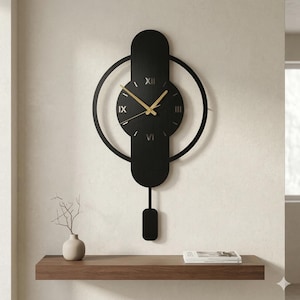 Könnte beinhalten: Eine moderne schwarze Wanduhr mit goldfarbenen Zeigern und römischen Ziffern. Die Uhr hat ein einzigartiges Design mit einem kreisförmigen Rahmen und einem pendelartigen Element. Sie ist an einer hellen Wand befestigt.