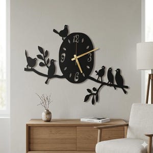 Puede incluir: Reloj de pared de metal negro con diseño de pájaros y ramas. La esfera del reloj es redonda con manecillas y números dorados. Varias siluetas de pájaros están posadas en las ramas, creando una pieza decorativa.