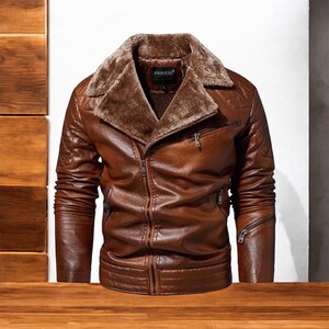 Può includere: Giacca in pelle marrone con colletto in ecopelliccia. La giacca ha una chiusura a zip, tasche multiple e dettagli trapuntati sulle spalle. La giacca è esposta su una superficie di legno.