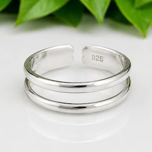 May include: A polished silver-tone open ring featuring a double-band design. The interior of the band is clearly stamped with the number 925, indicating the metal composition. The ring has a smooth, reflective surface and an adjustable gap.