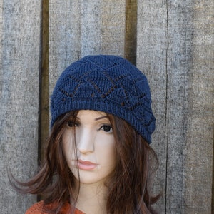 Op de afbeelding: Een donkerblauwe gebreide beanie met een kantpatroon. De beanie wordt gedragen door een persoon met lang bruin haar.