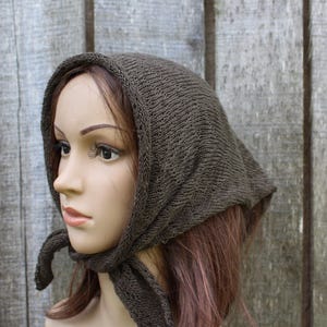 May include: A dark brown knitted headscarf featuring a triangular shape with a textured stitch pattern. The headscarf is tied securely under the chin with two knitted ends, covering the top and back of the head with a simple, functional design.
