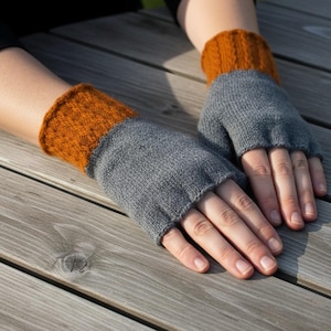 May include: A pair of gray and orange fingerless gloves. The gloves are made of a knitted material. The cuffs are orange, and the main body of the gloves is gray. The gloves are designed to keep hands warm while leaving the fingers free.