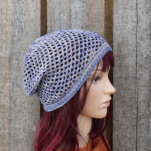 May include: A blue and white crocheted beanie with a loose, open weave. The beanie is worn on a mannequin with long, dark red hair.