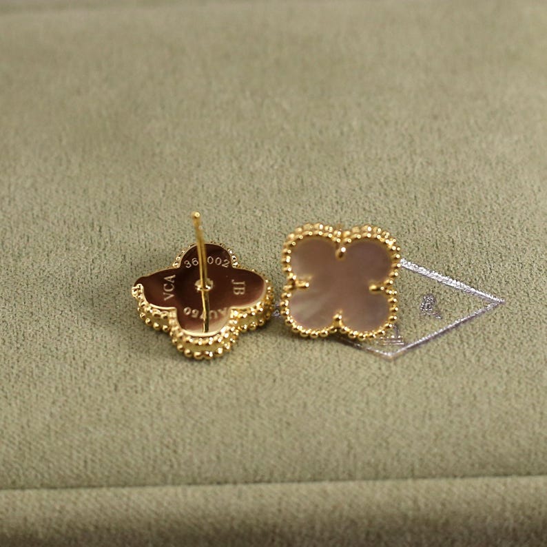 K&ouml;nnte beinhalten: Ein Paar goldfarbene Ohrstecker in Kleeblattform. Jeder Ohrring hat ein vierbl&auml;ttriges Kleeblatt-Design mit einem Perlmutt-Mittelteil und einem Perlenrand. Die Ohrringe haben einen Stecker- und Verschluss.