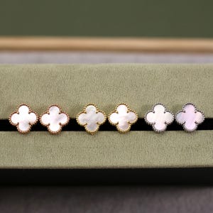 K&ouml;nnte beinhalten: Sechs Paar Ohrstecker in Kleeblattform mit Perlmutt-Mittelst&uuml;cken. Die Ohrringe sind in drei verschiedenen Metallausf&uuml;hrungen erh&auml;ltlich: Ros&eacute;gold, Gelbgold und Silber. Die Ohrringe werden auf einer gr&uuml;nen Oberfl&auml;che pr&auml;sentiert.