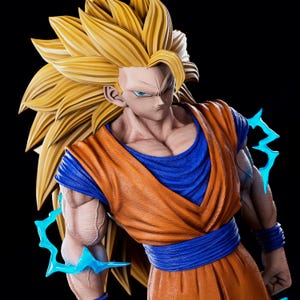 Puede incluir: Figura detallada de un personaje con pelo dorado puntiagudo y ojos azules. La figura viste un atuendo naranja y azul con efectos de energía azul. La figura tiene una expresión decidida y un físico musculoso, sobre un fondo negro.