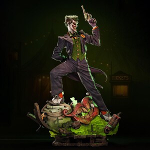 May include: A detailed statue of the Joker, a DC Comics villain, holding a gun. The figure is dressed in a purple suit, green vest, and orange-trimmed shirt. The statue stands on a base with a grinning mouth, money bags, and a sign that says "TICKETS."