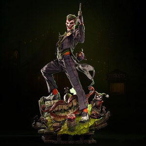 May include: A detailed statue of the Joker, a DC Comics villain, in a dynamic pose. The figure wears a purple suit, green hair, and white face paint. He holds a gun and stands on a themed base with Harley Quinn and other elements.