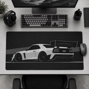 May include: A rectangular black desk mat featuring a white graphic illustration of a sports car viewed from the rear three-quarter angle. The car design includes a large rear spoiler, wide fenders, and a logo on the back panel. The mat is positioned on a desk.