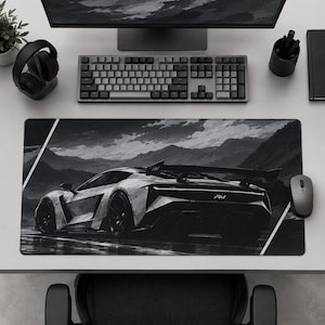 May include: A rectangular desk mat featuring a black and white illustration of a sports car with a rear spoiler and the text RM on the back, set against a mountainous landscape with a cloudy sky and diagonal white lines in the corners.