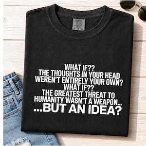 May include: A black crew neck t-shirt featuring white text that reads: WHAT IF?? THE THOUGHTS IN YOUR HEAD WEREN'T ENTIRELY YOUR OWN? WHAT IF?? THE GREATEST THREAT TO HUMANITY WASN'T A WEAPON... ...BUT AN IDEA? The shirt has a Comfort Colors brand label.