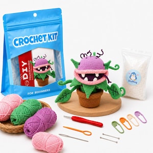 May include: A crochet kit for beginners featuring a blue plastic bag with the text CROCHET KIT, a finished purple and green plant in a brown pot, four balls of yarn in pink, green, and purple, a red crochet hook, needles, and colorful stitch markers.