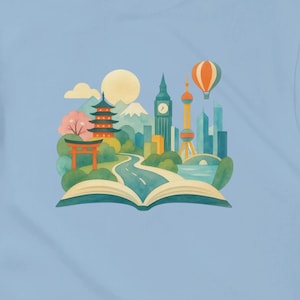 May include: A light blue t-shirt featuring a central graphic of an open book with a landscape emerging from its pages, including a pagoda, a clock tower, a hot air balloon, and a winding road, all rendered in a colourful, flat illustration style.