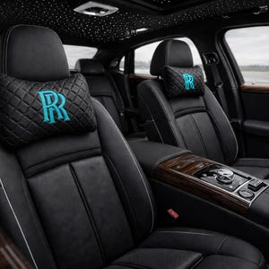 Könnte beinhalten: Innenansicht eines Luxusautos mit schwarzen Ledersitzen und Holzverkleidung. Die Kopfstützen haben ein Steppmuster und ein türkisfarbenes "R"-Logo. Der Autohimmel ist mit einem Sternenhimmel-Design versehen.