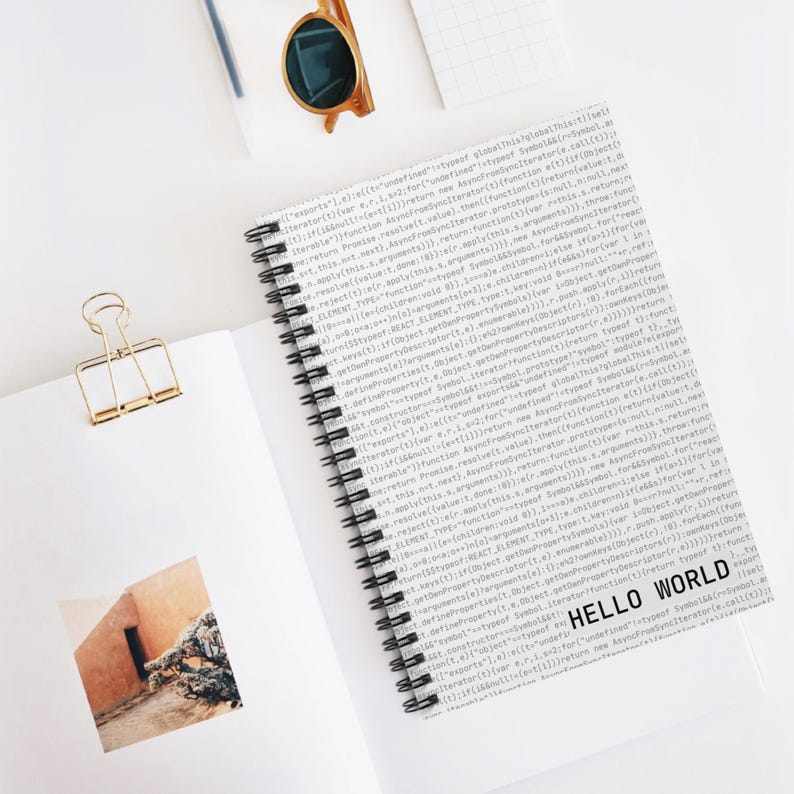 Minimalist white spiral notebook with ‘Hello World’ text and code pattern cover, developer-themed stationery on white desk.