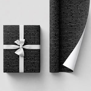 Pode incluir: Um presente embrulhado com papel de embrulho preto impresso com texto de código branco, amarrado com um laço de cetim branco. Ao lado, um rolo de papel de embrulho correspondente está parcialmente desenrolado, revelando o interior branco.