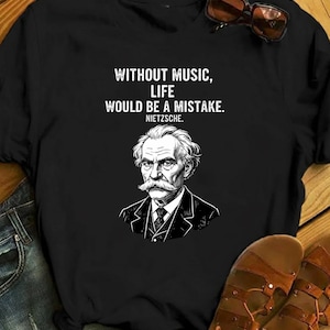 Könnte beinhalten: Schwarzes T-Shirt mit einem weißen Aufdruck von Friedrich Nietzsche und dem Zitat "OHNE MUSIK WÄRE DAS LEBEN EIN IRRTUM." Der Text und das Porträt sind weiß. Eine Sonnenbrille liegt auf dem T-Shirt. Geeignet für Musikliebhaber.