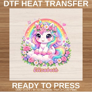 Peut inclure: Transfert thermique DTF coloré avec une licorne de dessin animé aux cheveux arc-en-ciel et une couronne de fleurs, avec le nom "Elizabeth". Le design comprend un arc-en-ciel, des nuages et des fleurs. Le texte dit "DTF HEAT TRANSFER" et "READY TO PRESS".