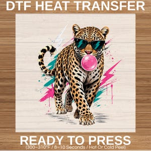 May include: A DTF heat transfer featuring a leopard wearing sunglasses and blowing a bubblegum bubble. The leopard is tan with black spots, and the background has teal and pink paint splatters. The text "READY TO PRESS" is at the bottom.