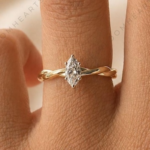 Op de afbeelding: Een gouden ring met een marquise-geslepen diamant. De band heeft een gedraaid touwontwerp. De ring zit om een vinger, tegen een zachte, neutrale achtergrond.