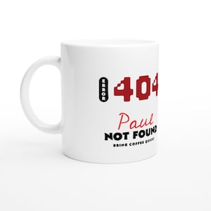 Può includere: Tazza da caffè in ceramica bianca con manico nero. La tazza presenta il testo "ERROR 404 Paul NOT FOUND BRING COFFEE QUICK!" in nero e rosso. La tazza è di dimensioni standard.