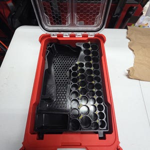 Puede incluir: Maleta de herramientas roja y negra abierta con tapa transparente. El interior presenta un inserto negro con varios compartimentos y soportes circulares. La tapa está abierta, revelando la organización interna. La maleta está diseñada para guardar herramientas.