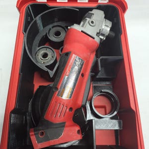 May include: A red and black power tool, possibly a grinder, is stored in a red case with black compartments. The case is open, showing the tool and its accessories. The tool has a silver head and a black handle.