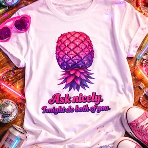 May include: White t-shirt with a vibrant pineapple graphic in shades of pink and purple. The text "Ask nicely. I might do both of you" is below the pineapple. Pink glitter sneakers and heart-shaped sunglasses are also visible.