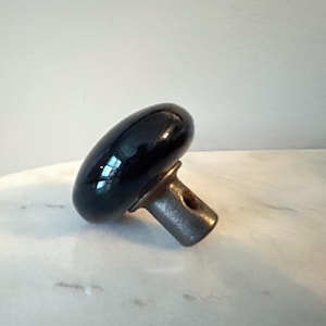 May include: A black, oval-shaped cabinet knob with a shiny, reflective surface. The knob is attached to a metal base with a small hole. The knob is likely for a drawer or cabinet door.