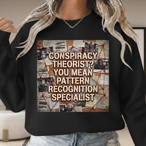 May include: Black sweatshirt with the text "CONSPIRACY THEORIST? YOU MEAN PATTERN RECOGNITION SPECIALIST" in a distressed font. The graphic features a corkboard with newspaper clippings and red string connecting them.