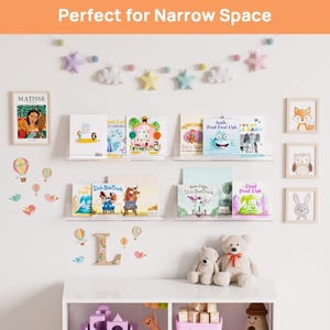 May include: Four clear acrylic floating wall shelves holding children's books, arranged in two rows. The wall features a star and cloud garland, framed art prints of a person, fox, owl, and rabbit, plus hot air balloon and bird wall decals.