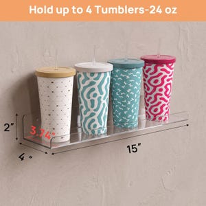 May include: A clear acrylic wall-mounted shelf holding four 24 oz tumblers with lids and straws. The shelf measures 15 inches wide, 4 inches deep, and 2 inches high, with a 3.74 inch depth capacity. The tumblers feature various patterns.