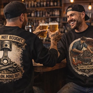 Könnte beinhalten: Zwei Männer in schwarzen Sweatshirts stoßen mit Biergläsern an. Auf einem Sweatshirt ist ein Kolben mit dem Text "BUILT, NOT BOUGHT" und "HANDS ON. MIND OFF" abgebildet. Das andere zeigt einen Mechaniker an einem Auto mit dem Text "THAT'S MUSIC".