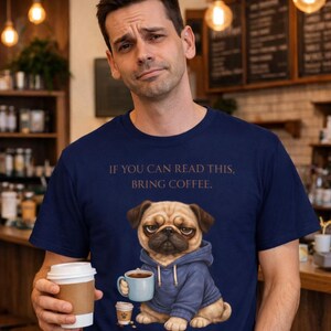Könnte beinhalten: Marineblaues T-Shirt mit dem Text "IF YOU CAN READ THIS, BRING COFFEE." Das Shirt zeigt eine Grafik eines Mops mit blauem Kapuzenpullover und einer Kaffeetasse. Die Person im Bild hält einen Kaffeebecher.