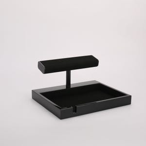 May include: A black jewelry display stand with a rectangular base and a T-shaped top. The top is covered in black velvet. The stand is designed to hold and showcase jewelry items.