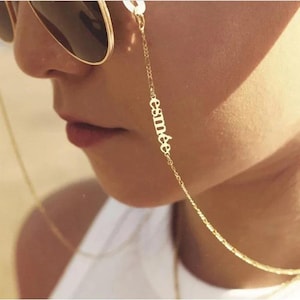 May include: A gold-coloured eyeglass chain with the name "esmée" in small letters. The chain is attached to the sunglasses and hangs down. A fashionable accessory to keep glasses secure.
