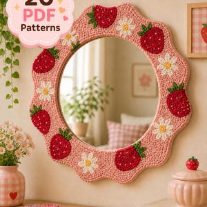 Puede incluir: Un espejo redondo con borde festoneado que presenta un marco de ganchillo rosa decorado con fresas rojas y margaritas blancas. Una insignia rosa en la esquina superior izquierda muestra el texto 20 PDF Patterns en letras marrón oscuro y rosa.