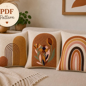 Puede incluir: Tres cojines cuadrados de tela texturizada color crema. El cojín izquierdo presenta un arco color mostaza y líneas de arcoíris. El central muestra un arco terracota con bordados florales. El derecho tiene un diseño de arcoíris.