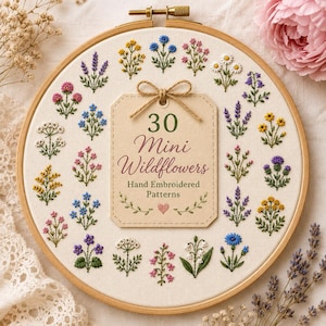 May include: A circular wooden embroidery hoop containing off-white fabric with various small, colourful wildflower designs stitched around a central beige tag. The tag features the text 30 Mini Wildflowers Hand Embroidered Patterns.