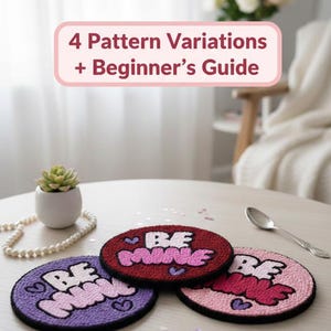 May include: Three round, handmade coasters with the words "BE MINE" in pink, on a table. The coasters are in shades of purple, red, and pink, with black borders. A small succulent in a white pot and a string of pearls are also on the table.