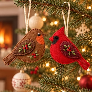 May include: Two felt bird ornaments hanging from a tree. One is a brown robin with an orange chest and embroidered floral details. The other is a bright red cardinal with a black face mask and dark red wing embroidery. Both have white cord loops.
