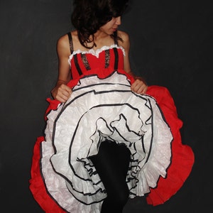 May include: A woman wearing a red and white dress with black trim. The dress has a large, ruffled skirt.